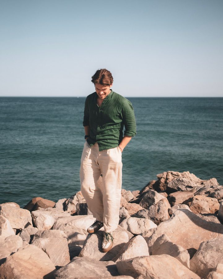 Felix standing on rocks at the edge of a grey sea, wearing a dark green jumper.